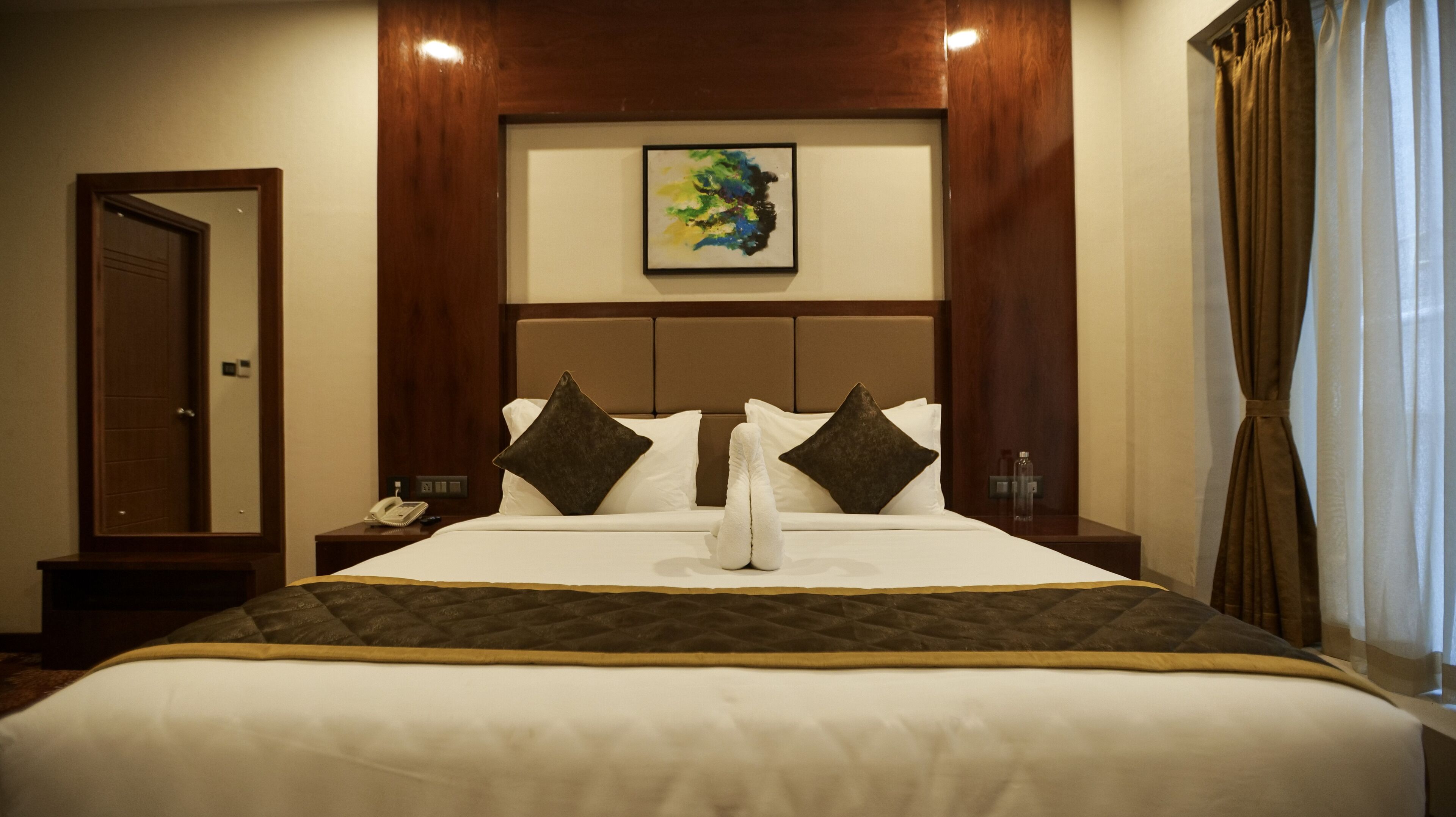 A hotel room with a large bed, a headboard with a framed artwork, a nightstand with a phone, and a door.