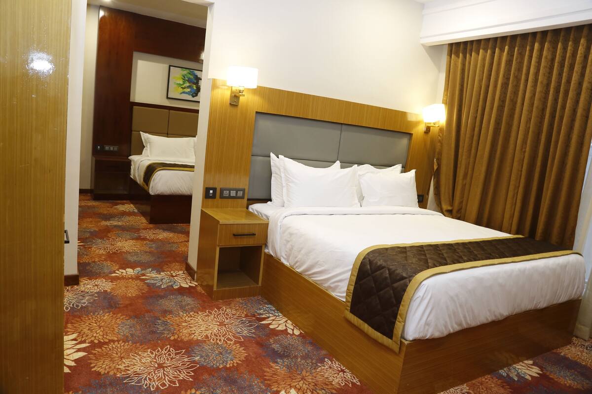 A hotel room with a large bed, a bedside table, a nightstand, and a wall-mounted lamp.
