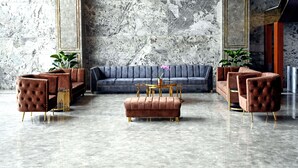 A modern lobby with a marble wall, a grey sofa, and brown tufted chairs. - Hotel Leroy Grand (Bengaluru)