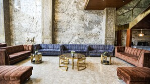 A spacious lounge with a blue sofa, gold-framed coffee tables, and a marble floor. - Hotel Leroy Grand (Bengaluru)