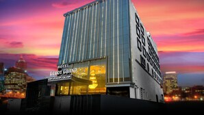 A modern hotel with a glass facade and illuminated signage. - Hotel Leroy Grand (Bengaluru)