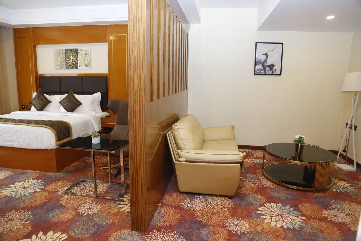 A hotel room with a bed, a sofa, a small table, and a decorative wall panel.