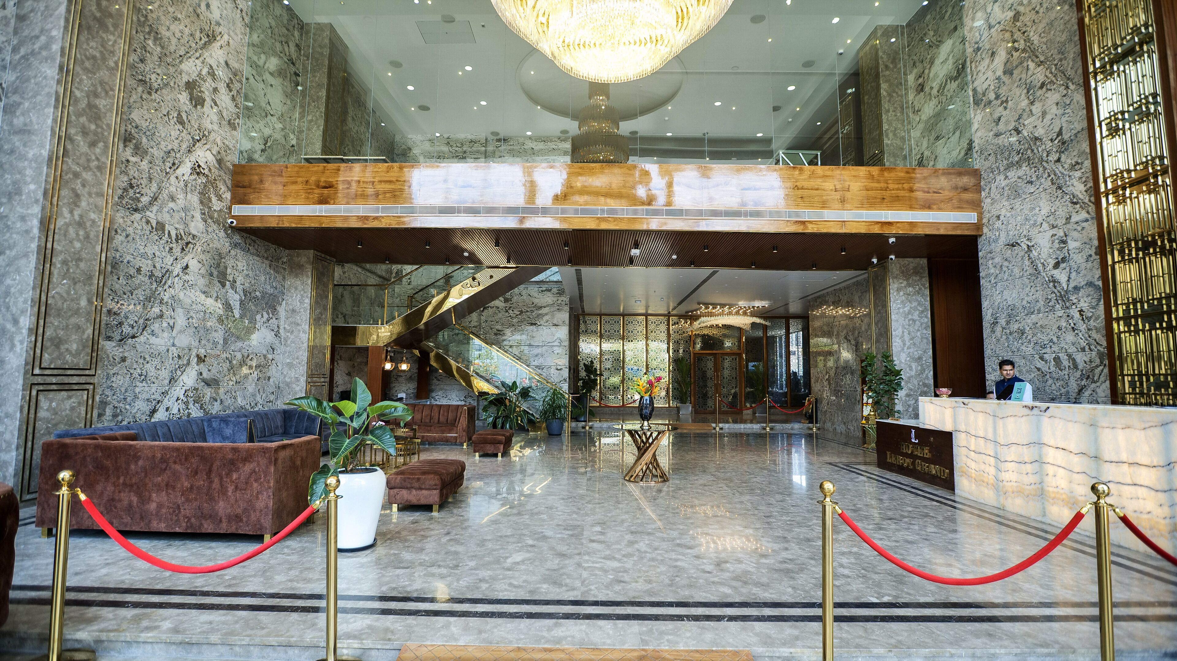 A luxurious lobby with marble floors, plush seating, a grand chandelier, and a modern staircase.