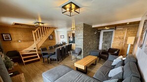 A modern living room with a wooden staircase, a dining area, and a stone accent wall.