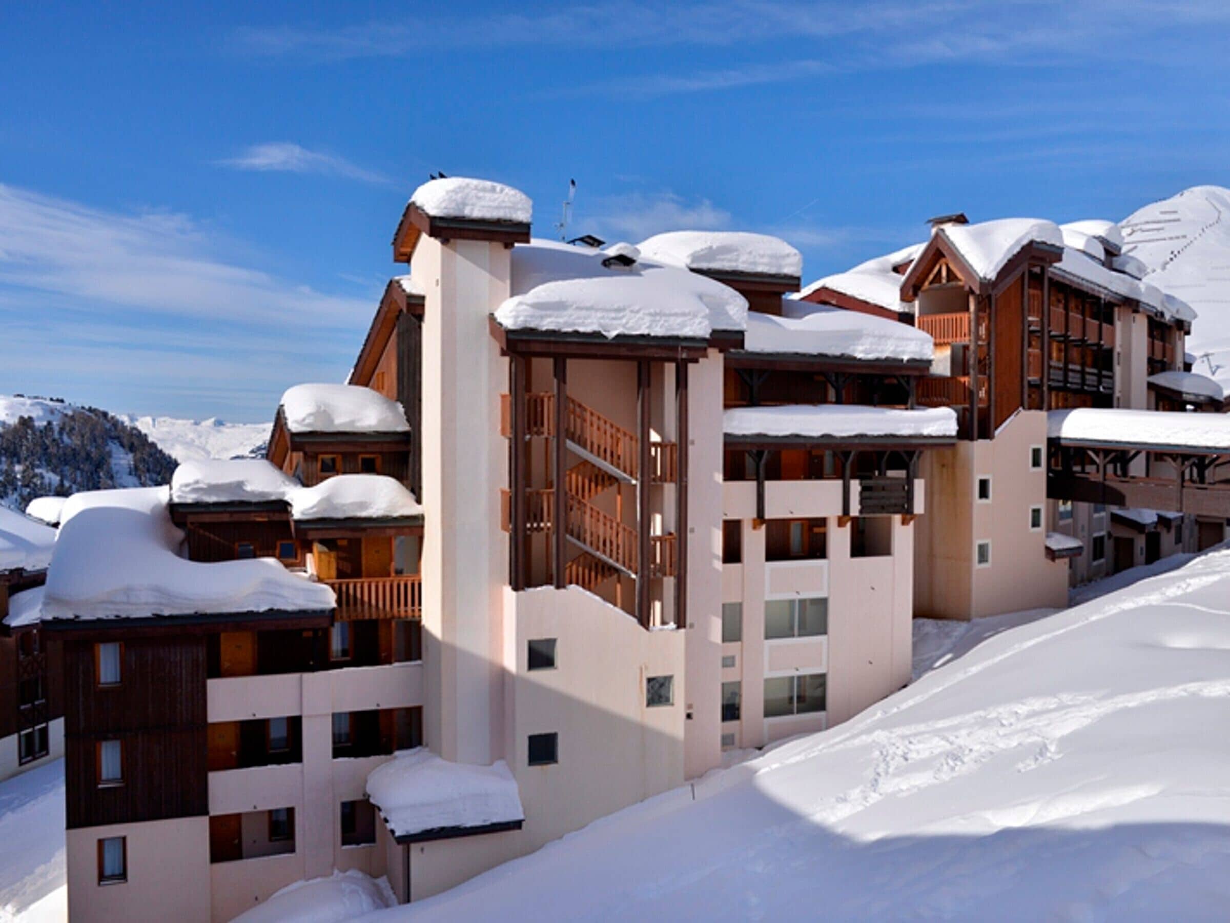 Ein schneebedecktes Mehrstöckiges Hotel mit Balkonen und Skipisten im Hintergrund.