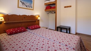 Ein Hotelzimmer mit einem hölzernen Kopfteil, einem Bett mit floraler Bettwäsche, einem kleinen Tisch und einer Wandablage mit gefalteten Handtüchern.