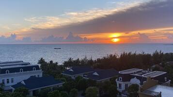 A coastal view with a sunset, buildings, and a boat on the water.