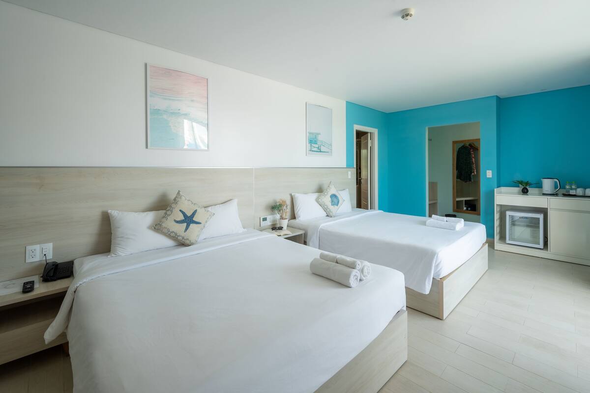 A hotel room with two beds, a small kitchenette, and a bathroom visible through an open door.