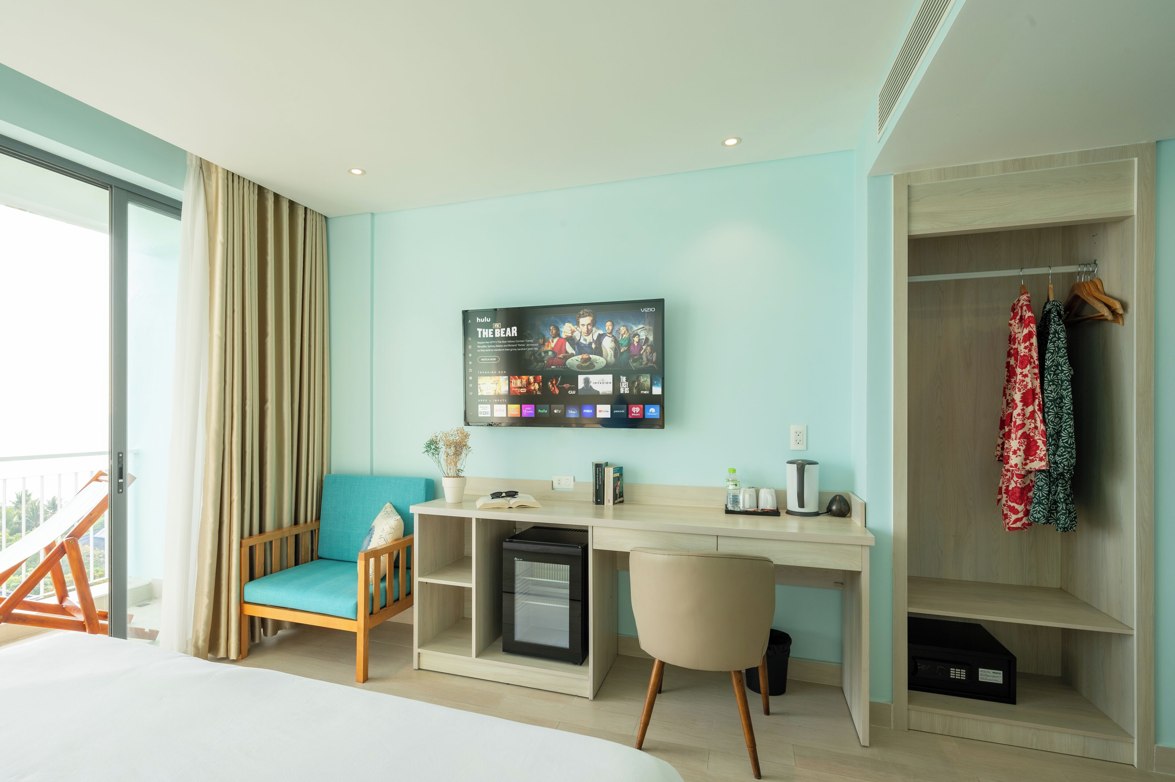 Ein Hotelzimmer mit Bett, Schreibtisch mit Computer, Fernseher, Kleiderschrank und Balkon.