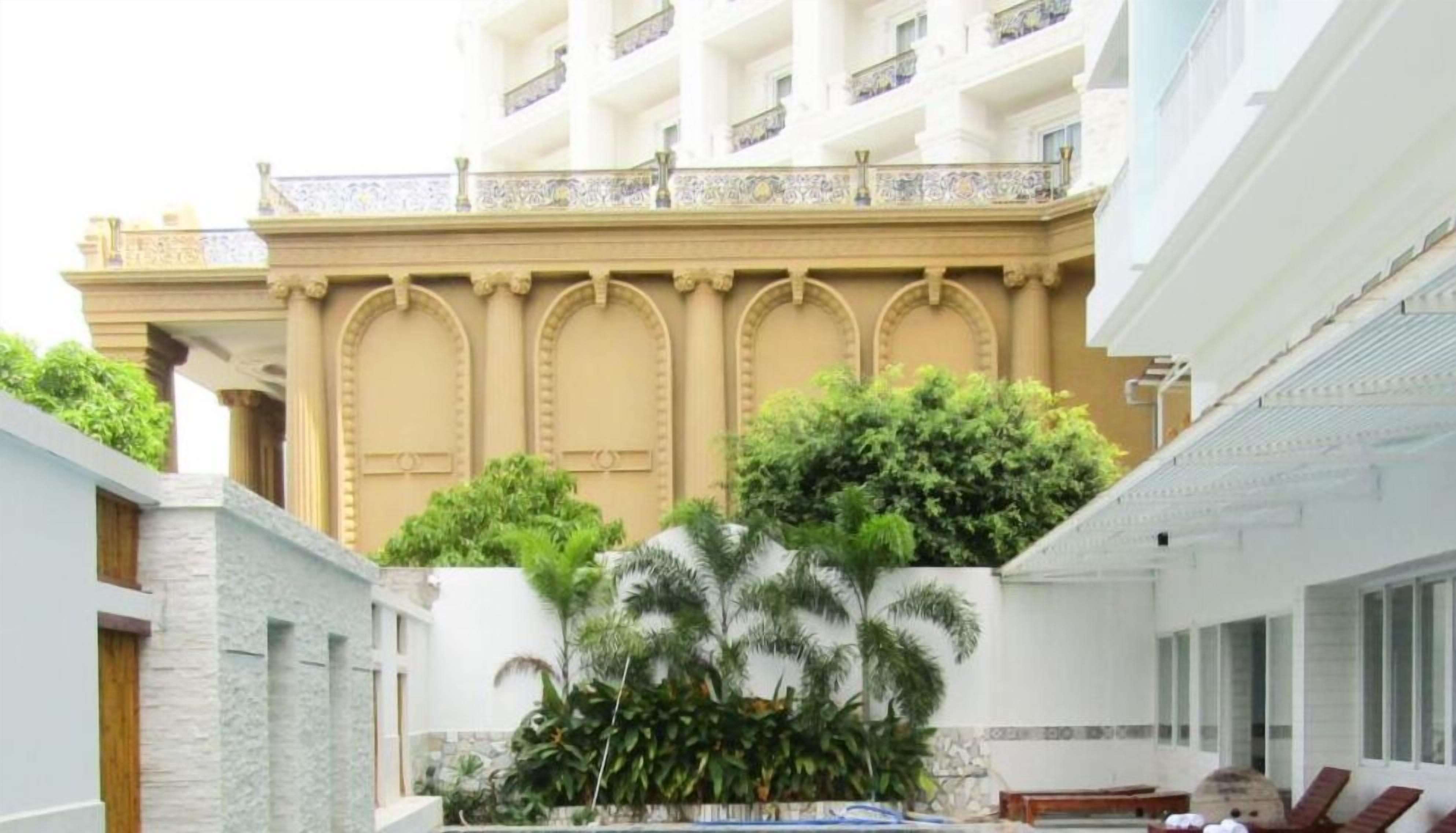 A hotel courtyard with a pool, palm trees, and a building with arched doorways.