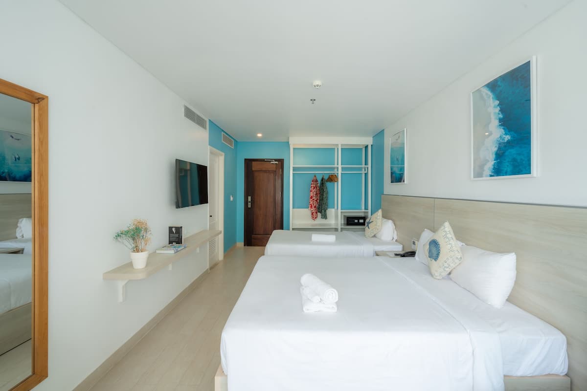A hotel room with two beds, a TV, a mirror, and a blue wall.