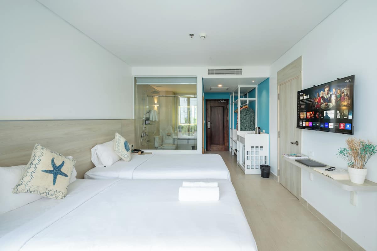 A hotel room with two beds, a TV, a bathroom, and a view of the outside.