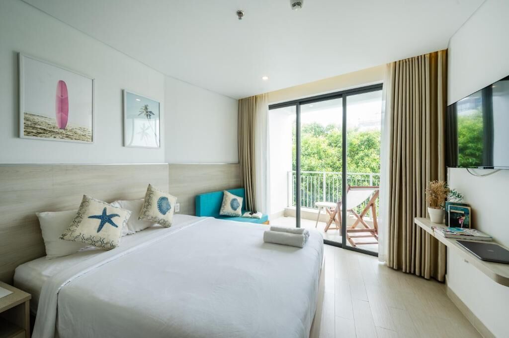 A modern hotel room with a large bed, a balcony with a view, and a flat-screen TV on the wall.
