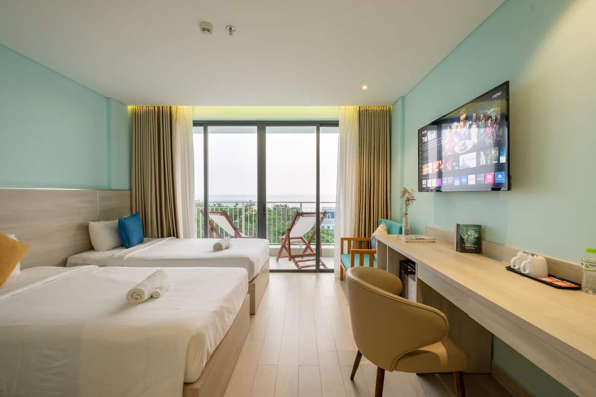 A hotel room with two beds, a desk, a TV, and a balcony with a view.