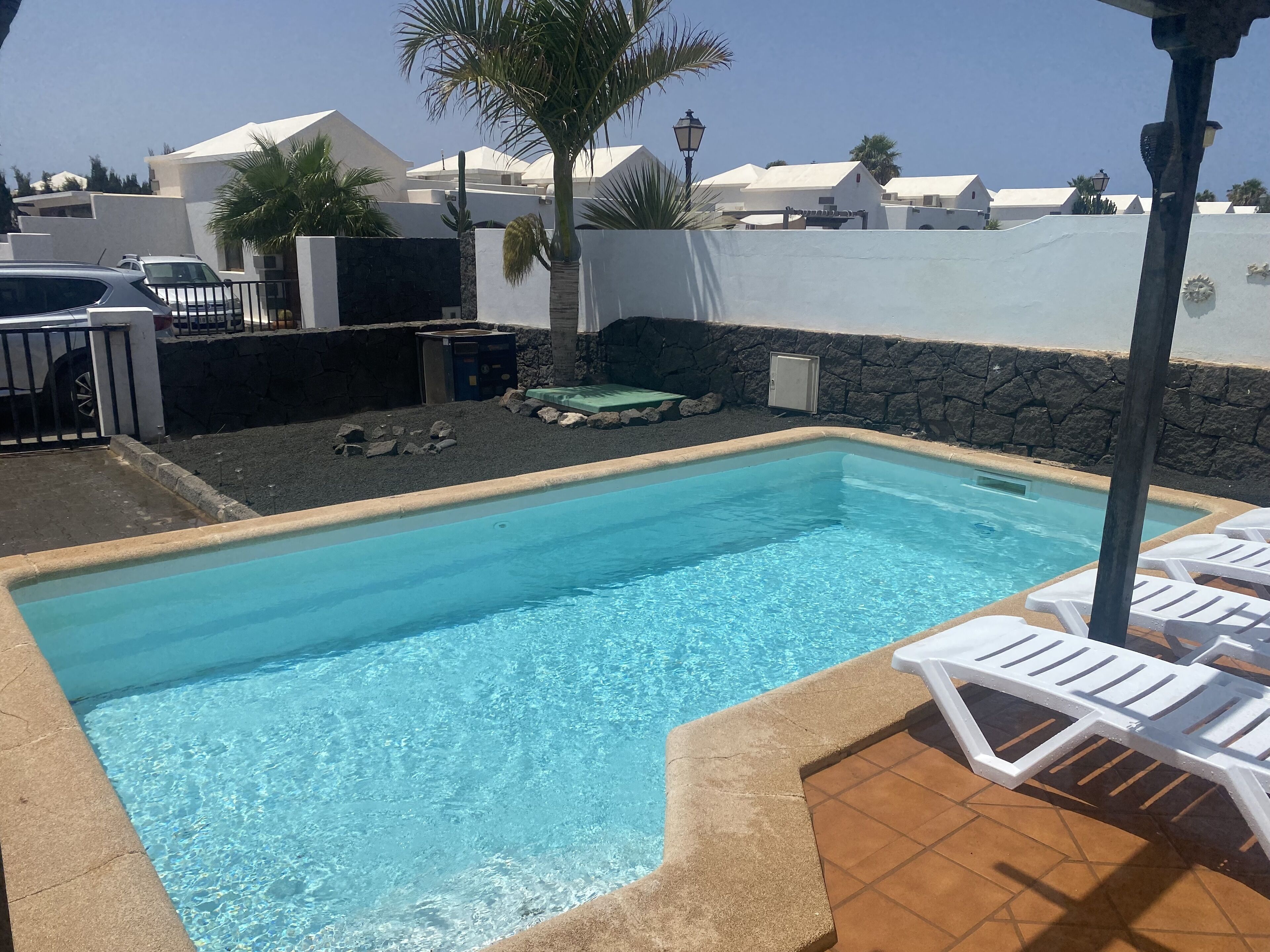 A swimming pool with clear blue water, surrounded by white lounge chairs and a stone wall.