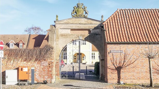A traditional European building with a tiled roof, a stone archway, and a sign indicating a historical site. - Lovely apartment in Barth with WiFi (Barth)