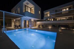 A modern house with a swimming pool, outdoor seating, and a stone wall. - Lilium Luxury Villa (By Xenias Villas) (Καλαθάς)