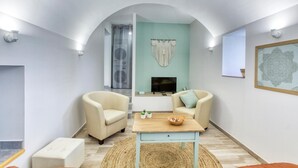 Een moderne woonkamer met twee beige fauteuils, een houten salontafel, een televisie en een decoratieve macramé wandhanger.