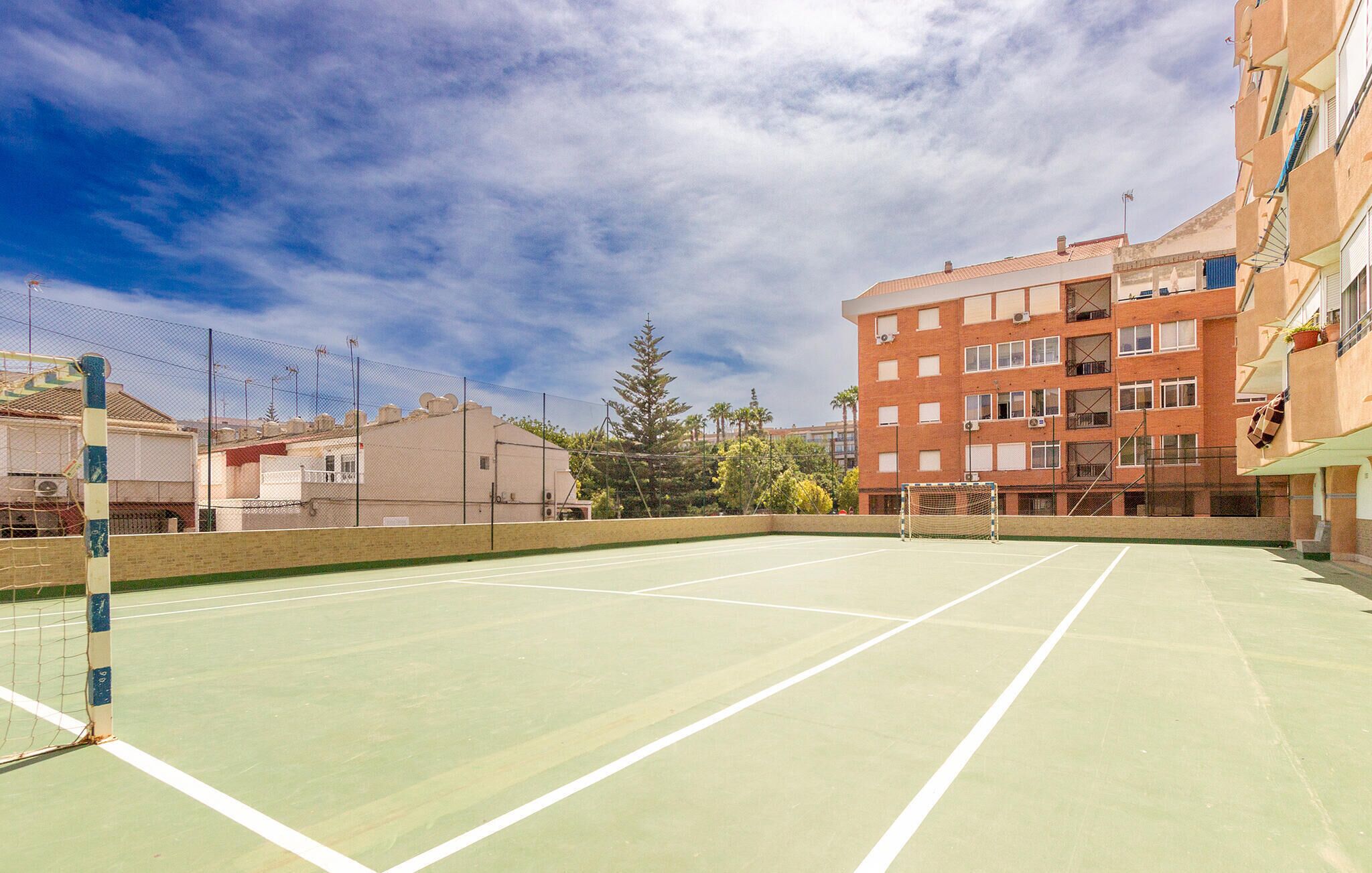 Ein Tennisplatz im Freien mit Netz, umgeben von Gebäuden und Bäumen.