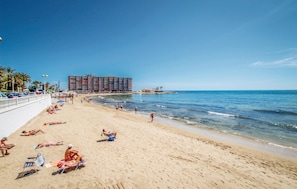 A beach with people sunbathing and swimming, a large hotel building in the background, and a clear blue sky. - Nice apartment in Torrevieja (Torrevieja)