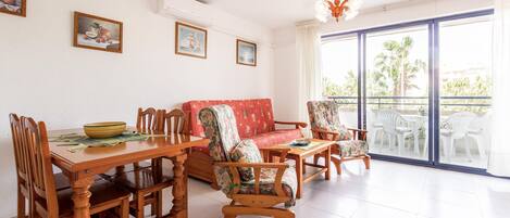 A dining area with a wooden table and chairs, a red sofa, and a balcony with white chairs.