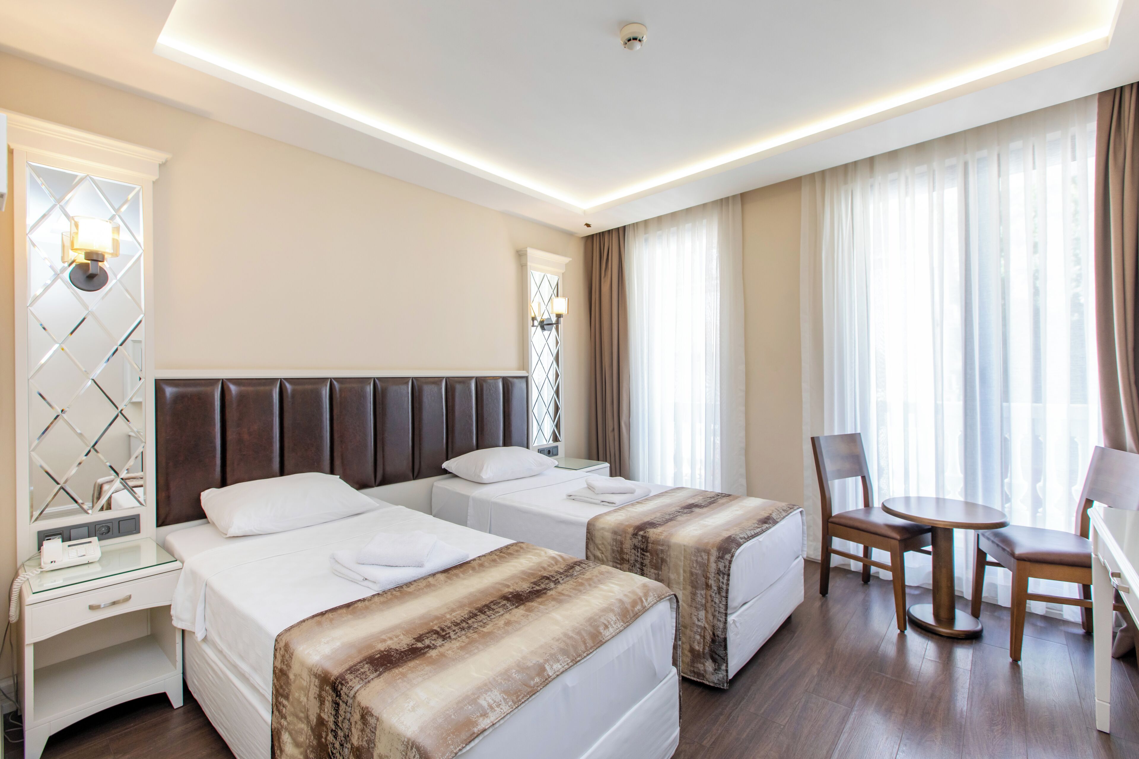 A hotel room with two beds, a desk, a chair, and a table.