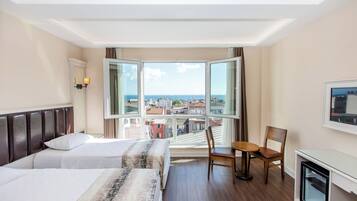 A hotel room with two beds, a small table, a chair, a TV, and a large window with a city view.