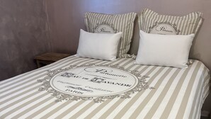 Una cama con una colcha a rayas y almohadas, una mesita de noche de madera y una pared con una lámpara decorativa.
