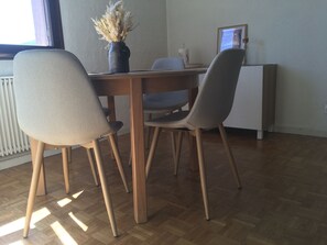 Et spiseområde med et træbord, fire stole, en vase med tørrede planter og en radiator.