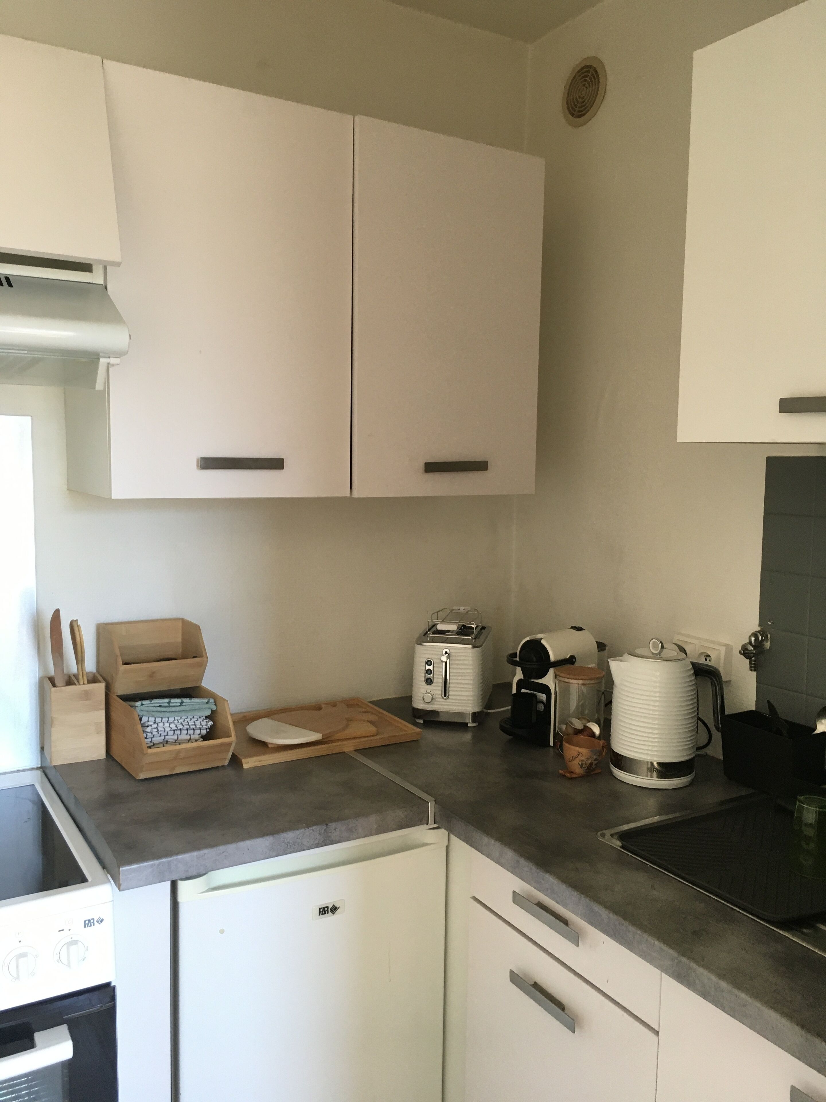 A kitchen with white cabinets, a toaster, a kettle, and a coffee maker on the countertop.