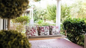 A covered porch with a swing seat and cushions, surrounded by greenery and a view of the outdoors. - Stylish Family 3BR Stay | Pets Allowed (Montgomery)