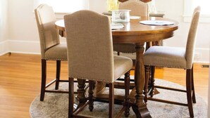 A dining room with a round wooden table, four upholstered chairs, a large wall clock, and a chandelier. - Stylish Family 3BR Stay | Pets Allowed (Montgomery)