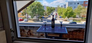 Vista desde una ventana mostrando una calle con una mesa que tiene una botella y una copa de vino.