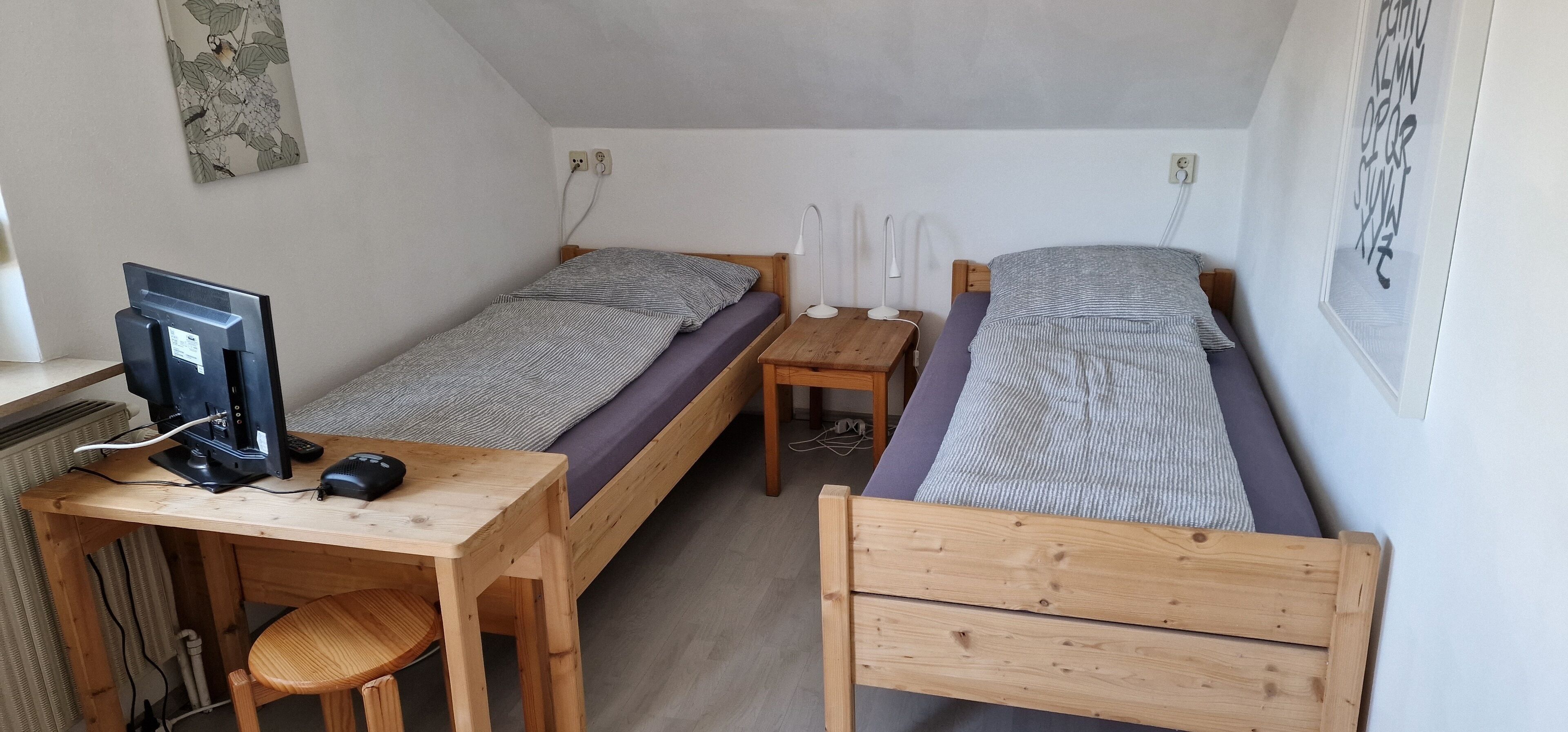 Un petit logement composé d’une seule pièce, comprenant deux lits simples, un bureau avec un ordinateur et une chaise.
