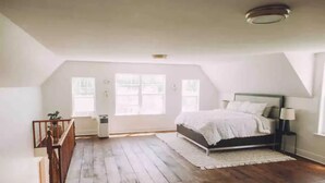 A bedroom with a wooden floor, a bed with white bedding, a nightstand, and a window. - 5 bdrm Farmhouse. Close to the beach. (Kensington)
