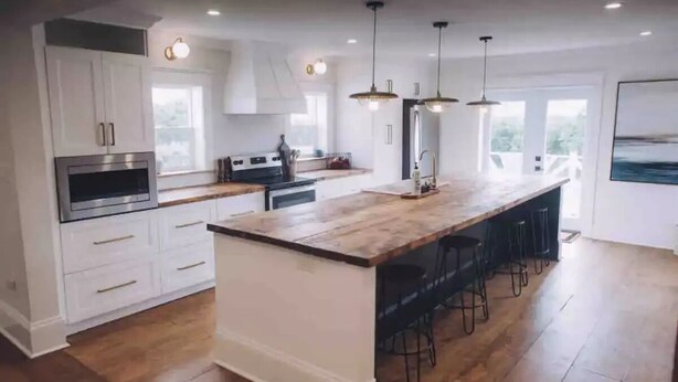 A modern kitchen with white cabinetry, a large island with bar stools, and pendant lighting. - 5 bdrm Farmhouse. Close to the beach. (Kensington)