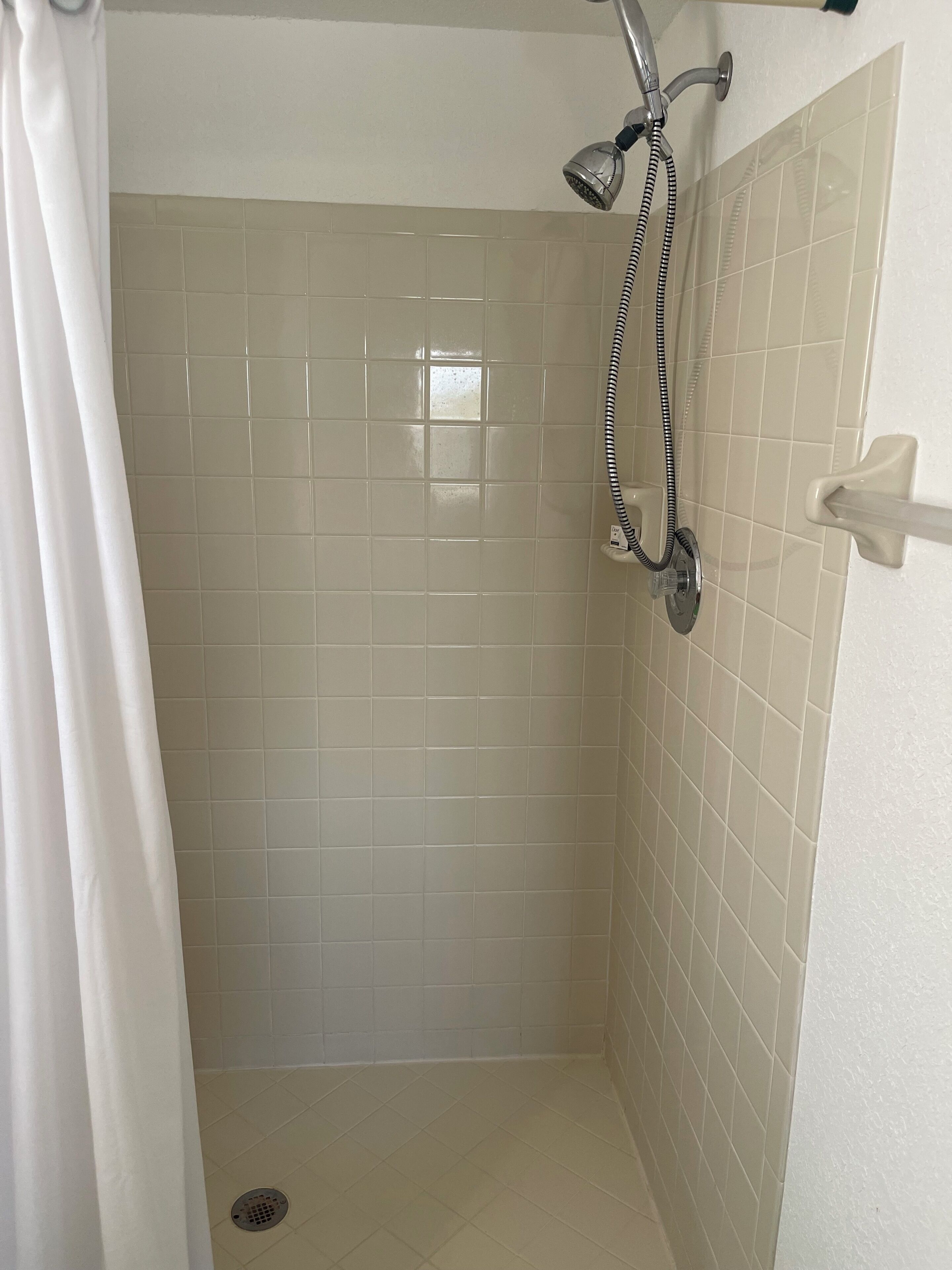 Een douche met beigetegels, een douchekop en een gordijn.