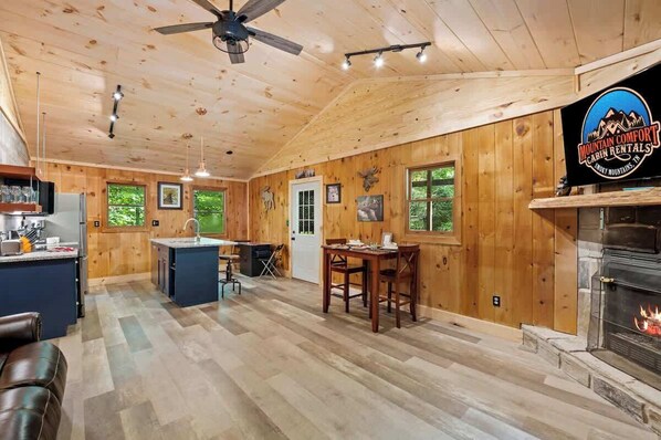 A cabin interior with a kitchen, dining area, and fireplace.