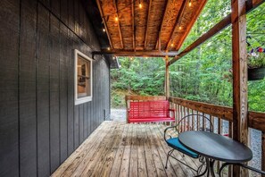 Une terrasse en bois avec un banc rouge et une table, donnant sur une zone boisée.