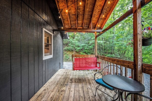 A wooden deck with a red bench and a table, overlooking a forested area.