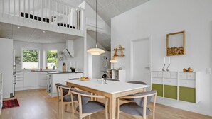 Une cuisine moderne avec des meubles blancs, un coin repas doté d’une table et de chaises en bois, et une vue sur l’extérieur par une fenêtre.