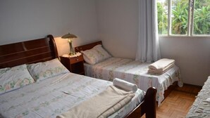 A room with two beds, a nightstand with a lamp, a window with curtains, and a view of greenery outside. -  Pousada Barão Real (Sao Lourenco)