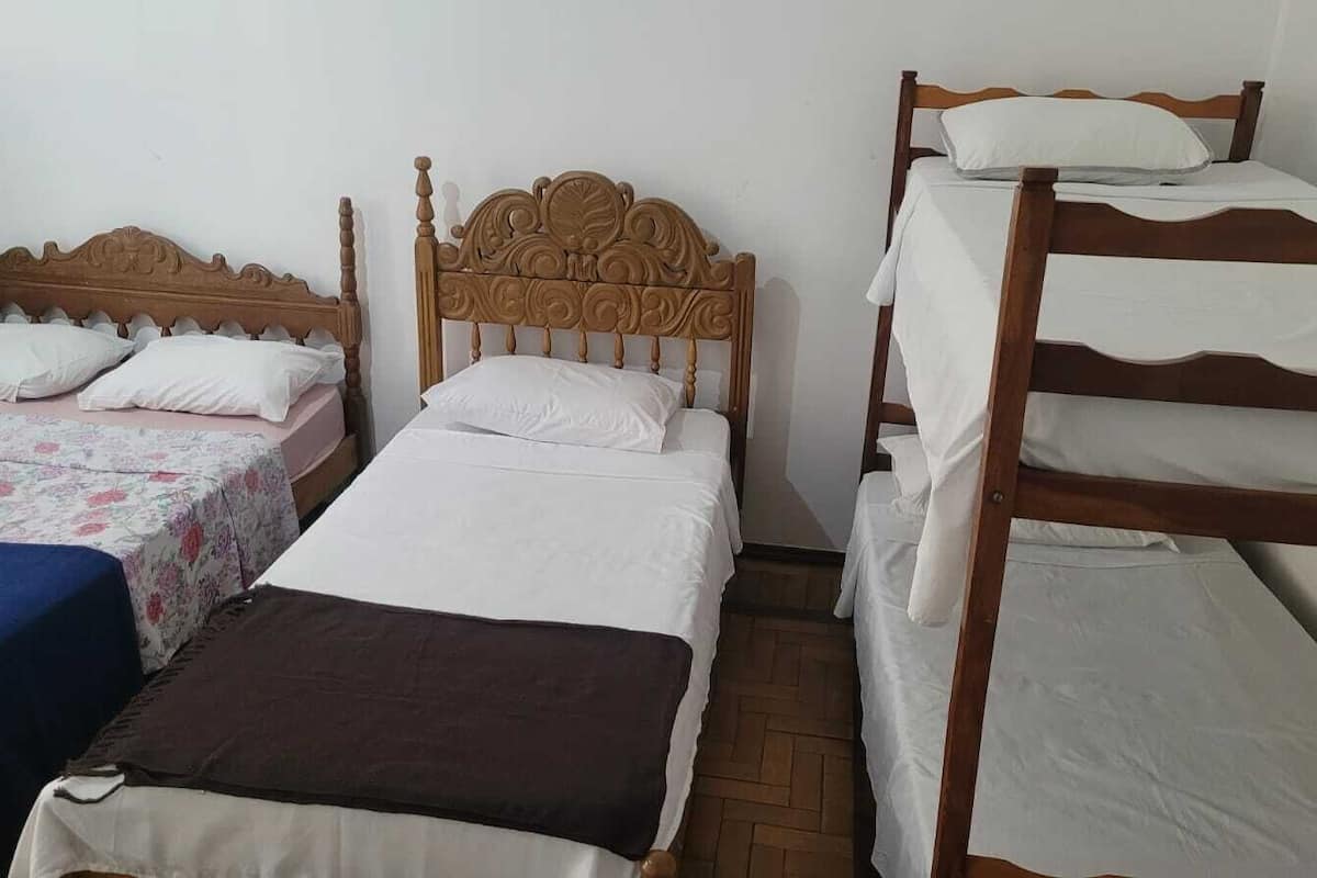 Ein Zimmer mit zwei Einzelbetten und einem Etagenbett, alles mit weißer Bettwäsche.