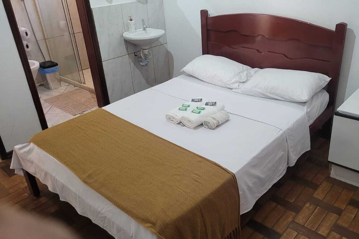 Ein Hotelzimmer mit Bett, Nachttisch, kleinem Kühlschrank, Spüle und Duschbereich.