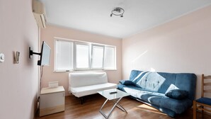 Ein modernes Wohnzimmer mit einem weißen Sofa, einem blauen Sofa, einem Glastisch und einem Holznachttisch.