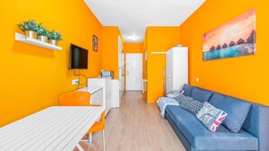 Una habitación luminosa de color naranja con un sofá, una mesa y un televisor.