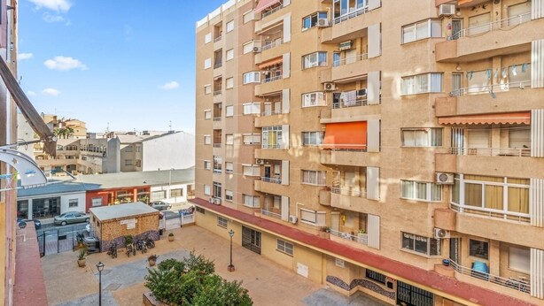 Un edificio residencial de varios pisos con balcones, un patio con asientos y una pequeña tienda.
