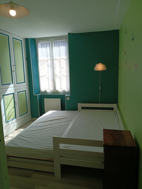 A room with a single bed, a window with curtains, a wall-mounted lamp, and a door with a green frame. - Gite les Glycines, 10 pers (+2bebes), 4bedroom, 2bathroom (Vicq-sur-Gartempe)