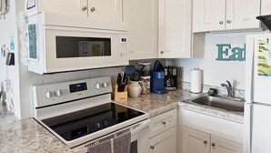 Une cuisine avec des meubles blancs, un four à micro-ondes, un four, un évier et une machine à café.