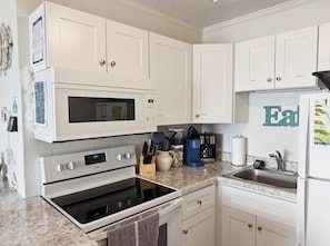 A kitchen with white cabinets, a microwave, an oven, a sink, and a coffee maker.